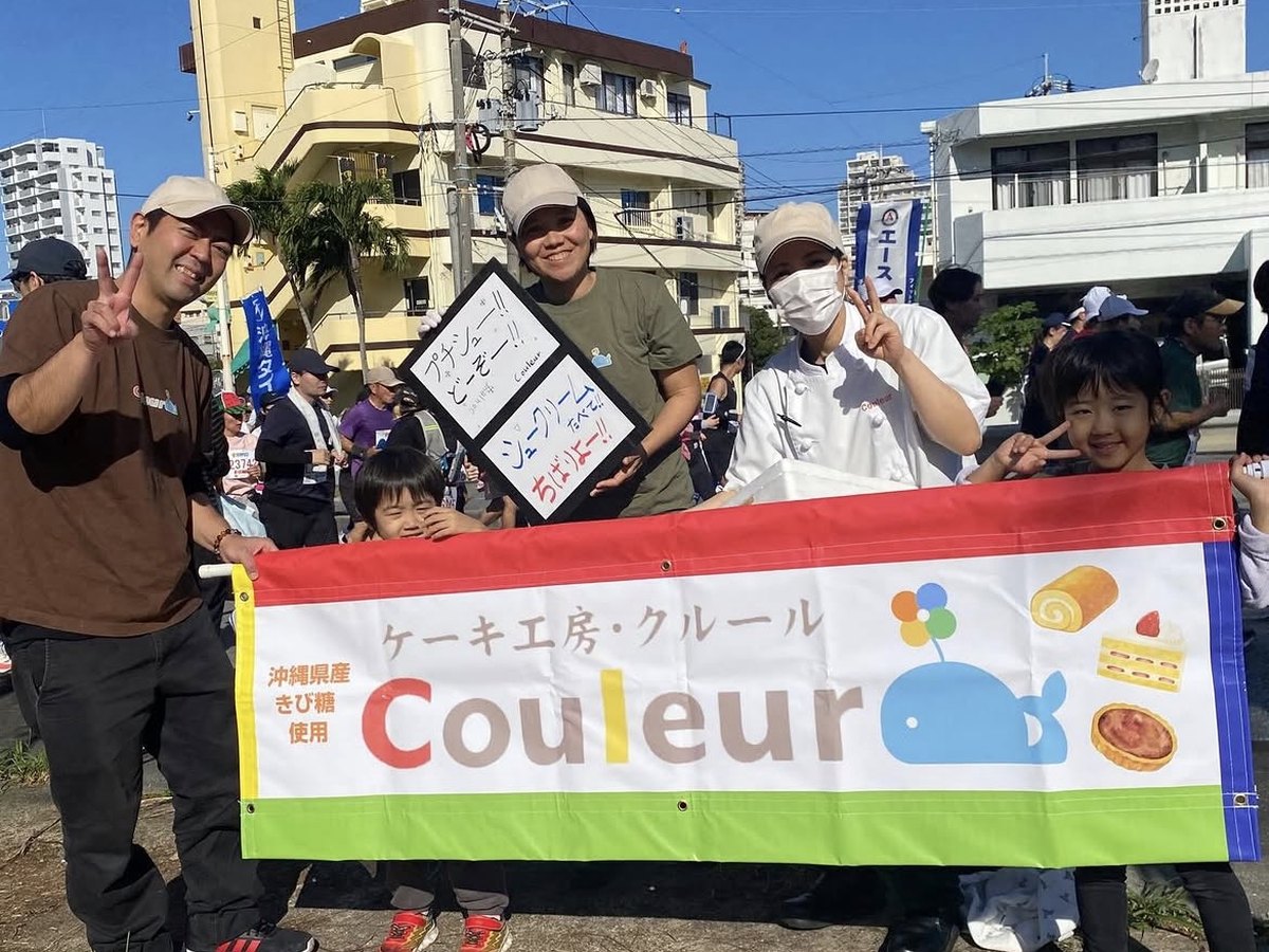 豊見城ハーリー大会でケーキ工房クルールの横断幕を掲げるスタッフ